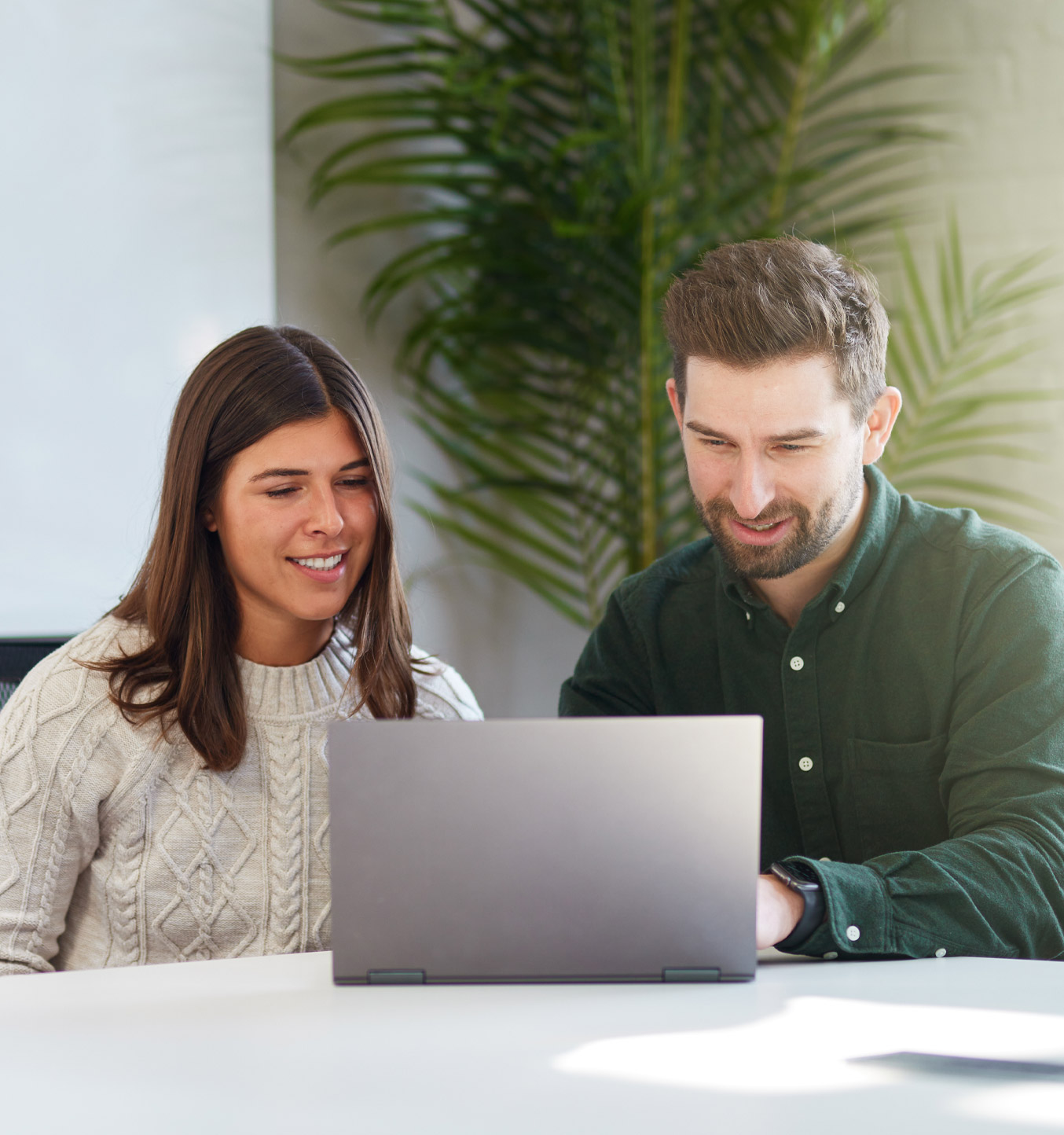 A man talking to his female co-worker while she types on a keyboard.